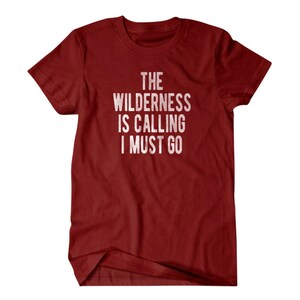 May include: Red t-shirt with white text that reads "The Wilderness is Calling I Must Go."
