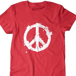 Puede incluir: Camiseta roja con un gr&aacute;fico de signo de paz blanco. El signo de paz est&aacute; rodeado de salpicaduras de pintura blanca.