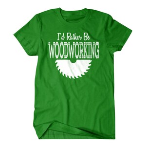 以下が含まれることがあります： 白い文字で「I'd Rather Be Woodworking」と書いてある緑色のTシャツ。白い鋸のシルエットが描かれている。