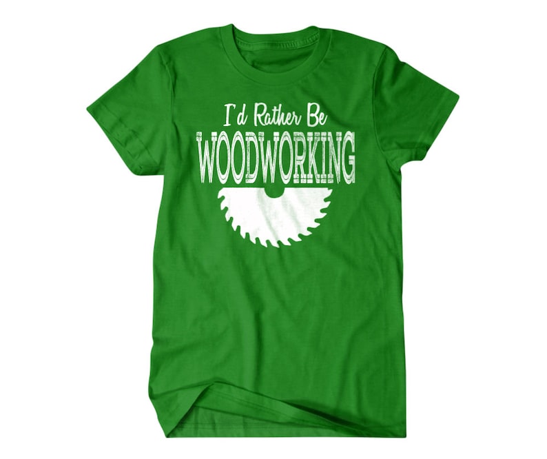 以下が含まれることがあります： 白い文字で「I'd Rather Be Woodworking」と書いてある緑色のTシャツ。白い鋸のシルエットが描かれている。