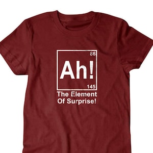 May include: A maroon t-shirt with a white graphic. The graphic features the word "Ah!" inside a white box, with the numbers 86 and 145 above and below. Below the box, the text reads "The Element Of Surprise!"