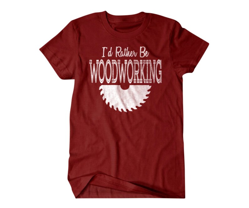 以下が含まれることがあります： 白い文字で「I'd Rather Be Woodworking」と書かれた赤いTシャツと、白い鋸刃のシルエット。