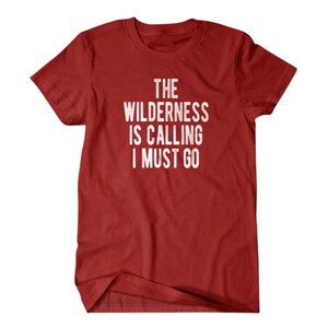 May include: Red t-shirt with white text that reads "The Wilderness is Calling I Must Go".
