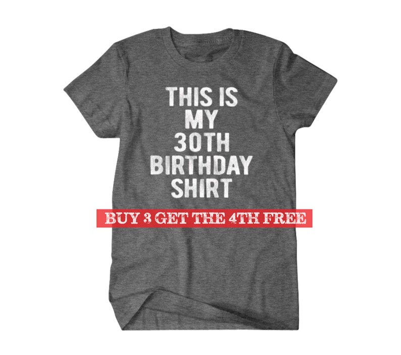 Puede incluir: Camiseta gris con texto blanco que dice "This is my 30th Birthday Shirt". La parte inferior de la camiseta tiene una pancarta roja que dice "Buy 3 Get the 4th Free".