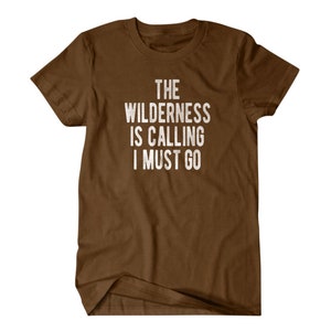 May include: Brown t-shirt with white text that reads "The Wilderness is Calling I Must Go."