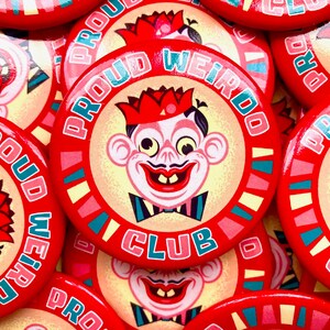 May include: A close-up of several red and white button pins with a cartoon character wearing a red hat and a bow tie. The text on the buttons reads "Proud Weirdo Club".