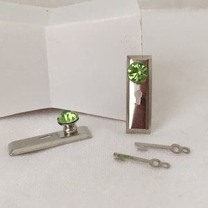 May include: Two miniature door hardware sets with green crystal knobs and keyholes. One set includes a door knob and a separate door plate. The other set includes a door knob and a separate door plate with a keyhole. Two silver keys are included.
