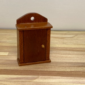 May include: A small, wooden cabinet with a single door and a knob. The cabinet is brown and has a slightly arched top.