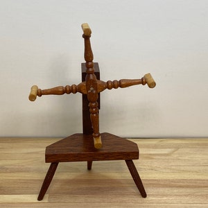 May include: A wooden yarn winder with four arms and a small base. The winder is made of dark brown wood with light brown accents. The base is a triangular shape with three legs.