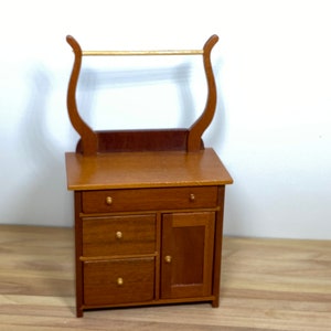 May include: A wooden dresser with three drawers and a cabinet door. The dresser has a decorative top with a gold rod.