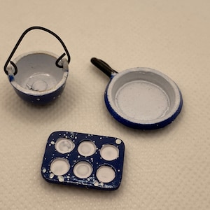 May include: Miniature blue and white speckled enamelware kitchen set. Includes a small pot with a wire handle, a frying pan, and a six-cup muffin tin. The set is designed for a dollhouse or miniature display.
