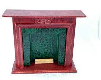 May include: A miniature wooden fireplace with a red painted finish and a green painted interior. The fireplace has a simple carved design on the mantel and a single log inside.
