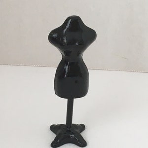 May include: A black mannequin torso with a stand. The mannequin is made of plastic and has a smooth, glossy finish.