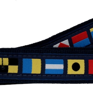 Puede incluir: Un cinturón azul marino con una hebilla dorada y un patrón de banderas náuticas coloridas. Las banderas están dispuestas en fila y son todas de diferentes colores y diseños.
