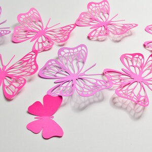 May include: A collection of eight pink and purple paper butterflies with intricate cut-out designs. The butterflies are arranged in a random pattern on a white background.
