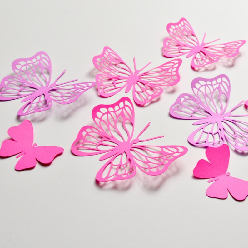 May include: A set of seven pink and purple paper butterflies with intricate cut-out designs. The butterflies are arranged on a white background.