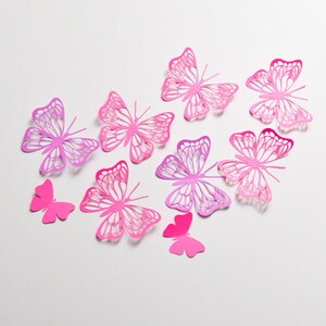 May include: A collection of eight pink and purple paper butterflies of varying sizes, arranged on a white background.