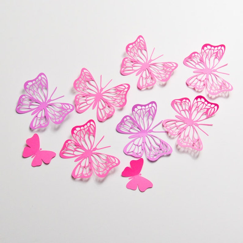 May include: A collection of eight pink and purple paper butterflies of varying sizes, arranged on a white background.
