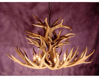 Può includere: Un grande lampadario in corna di cervo con un design rustico. Il lampadario è fatto di corna naturali e presenta una catena appesa al soffitto. Il lampadario ha più lampadine ed è acceso.
