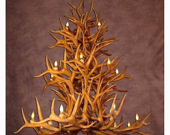 Può includere: Un grande lampadario di design intricato realizzato con corna di cervo. Il lampadario ha più livelli e presenta un caldo tono di legno naturale. È illuminato da più lampadine, creando un'atmosfera rustica ed elegante.