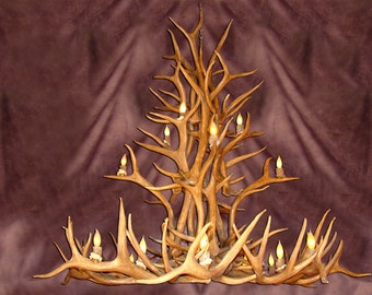 Può includere: Un grande lampadario rustico realizzato con corna naturali. Il lampadario presenta più luci a forma di candela con un'illuminazione giallo caldo. Le corna sono di colore marrone chiaro e l'apparecchio è appeso a una catena.