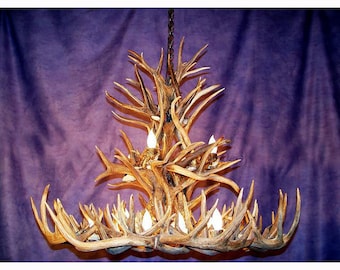May include: A large antler chandelier with multiple branches and lights. The chandelier is made of natural antlers and has a rustic, natural look.
