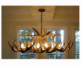 Può includere: Un lampadario fatto da una collezione di corna con più lampadine. Il lampadario è appeso a una catena in una stanza con finestre.