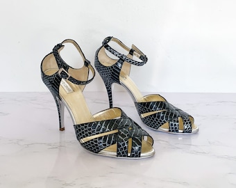 May include: A pair of black snakeskin heeled sandals with ankle straps. The sandals have a silver trim and the brand name "Sergio Rossi" is visible on the strap.