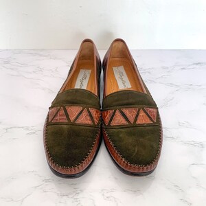 May include: A pair of green suede loafers with brown leather trim and a crocodile-embossed detail. The loafers are by the brand "May & Law".