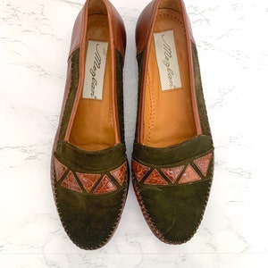 May include: A pair of brown leather loafers with green suede uppers and brown leather accents. The loafers have a pointed toe and a low heel. The brand name "Morgan" is printed on the inside of each shoe.