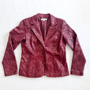 May include: A burgundy faux leather blazer with a textured finish. The blazer has a notched collar, two button closure, and long sleeves.