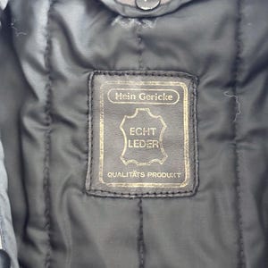 Op de afbeelding: Een bruin leren jack met een label met de tekst "Hein Gericke Echt Leder Qualit&auml;ts Produkt".