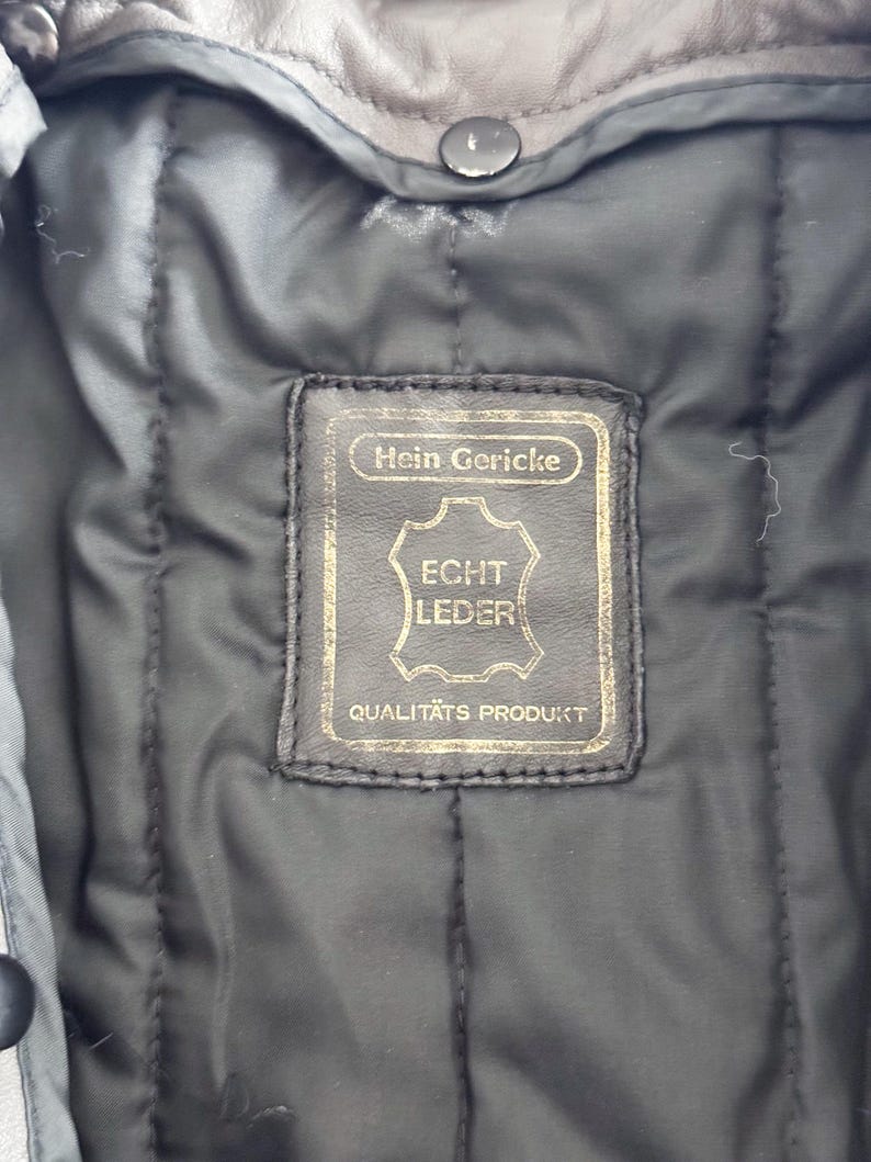 Op de afbeelding: Een bruin leren jack met een label met de tekst "Hein Gericke Echt Leder Qualit&auml;ts Produkt".