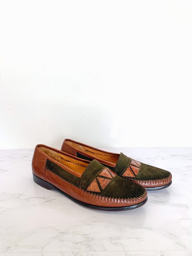 May include: A pair of brown leather loafers with green suede accents and geometric cutouts. The loafers have a pointed toe and a low heel.