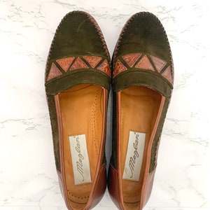 May include: A pair of green suede loafers with brown leather accents and the brand name "Meglan" on the inside.