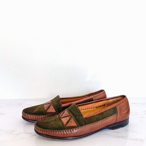 May include: A pair of brown leather loafers with green suede uppers and decorative brown leather accents. The loafers have a stitched edge and a brown leather sole.