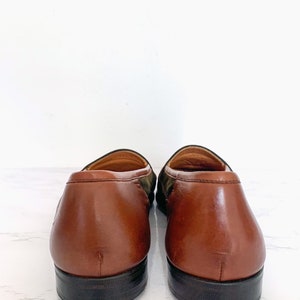 May include: A pair of brown leather loafers with a green and brown suede pattern on the back of the shoes.