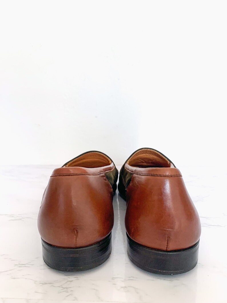 May include: A pair of brown leather loafers with a green and brown suede pattern on the back of the shoes.