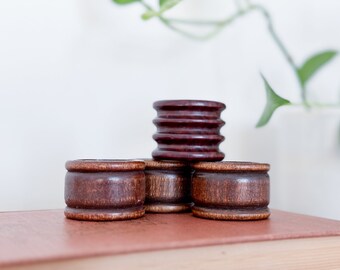 May include: Four wooden napkin rings, two are dark brown and two are a lighter brown. The rings are stacked on top of each other on a brown book.