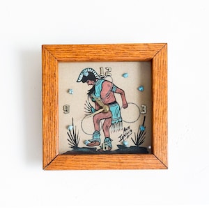 May include: A wooden framed clock with a Native American dancer illustration and turquoise accents. The clock face has Roman numerals and the artist's signature "Anita Ignacio" is visible.