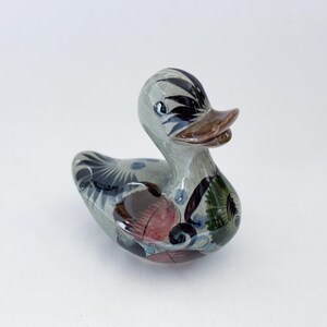 May include: Hand-painted ceramic duck figurine with blue, green, black, and brown accents. The duck has a white body and a brown beak.