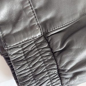 Op de afbeelding: Close-up van een zwart leren jack met een geribbelde elastische tailleband.