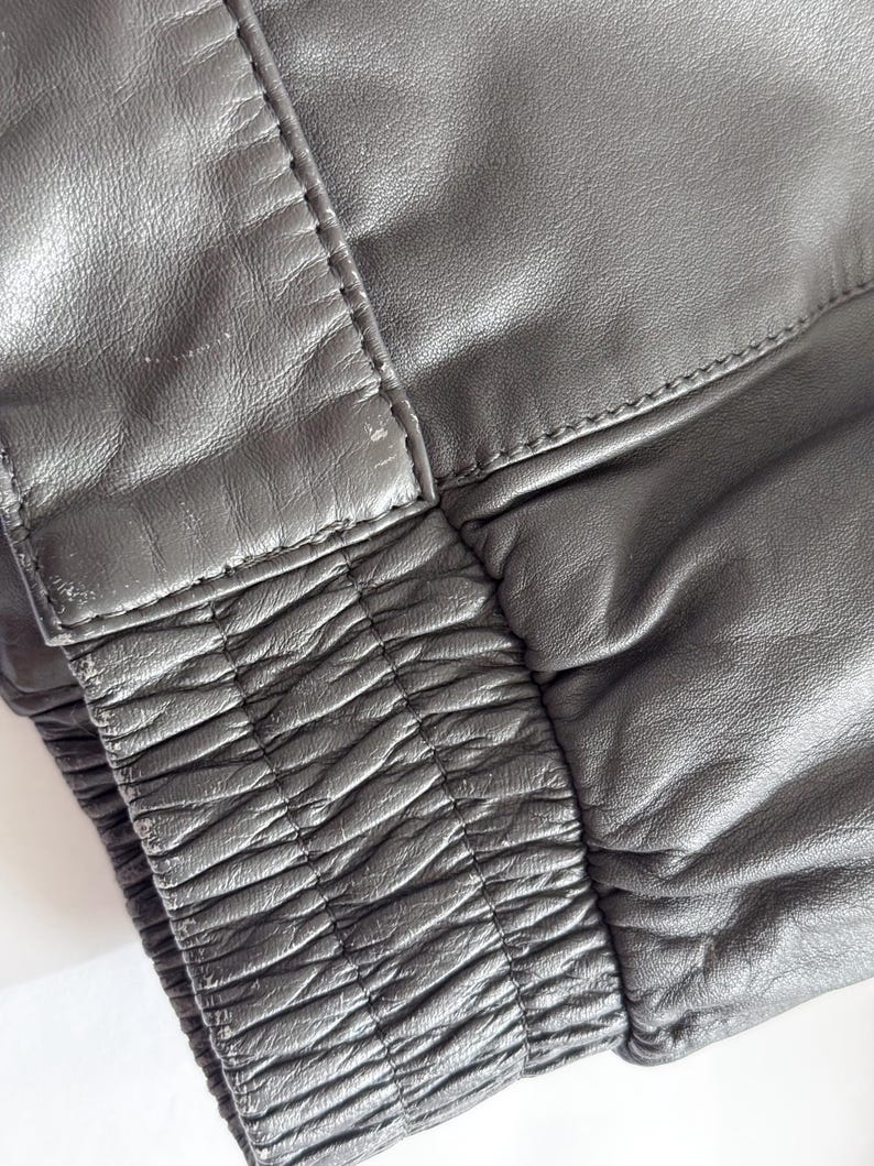 Op de afbeelding: Close-up van een zwart leren jack met een geribbelde elastische tailleband.