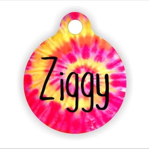 Könnte beinhalten: Runder Hundeanhänger im Tie-Dye-Muster mit dem Namen "Ziggy" in schwarzen Buchstaben.