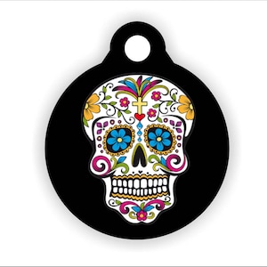 May include: A round black tag with a white sugar skull design. The skull is decorated with colorful flowers and swirls.
