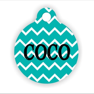 May include: A turquoise blue and white chevron patterned dog tag with the name "Coco" in black text.