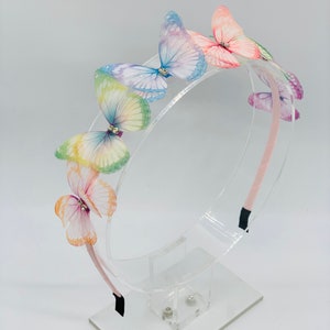Pu&ograve; includere: Un cerchietto rosa con decorazioni a farfalla arcobaleno. Le farfalle sono realizzate in tessuto trasparente e hanno ali iridescenti.