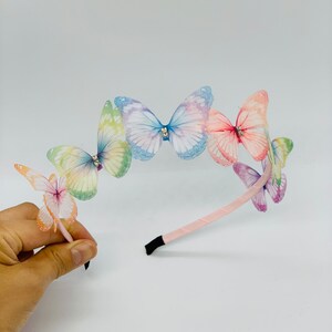 Pu&ograve; includere: Un cerchietto rosa con cinque fermagli per capelli a forma di farfalla iridescenti. Le farfalle sono in tonalit&agrave; di blu, rosa, verde e giallo.