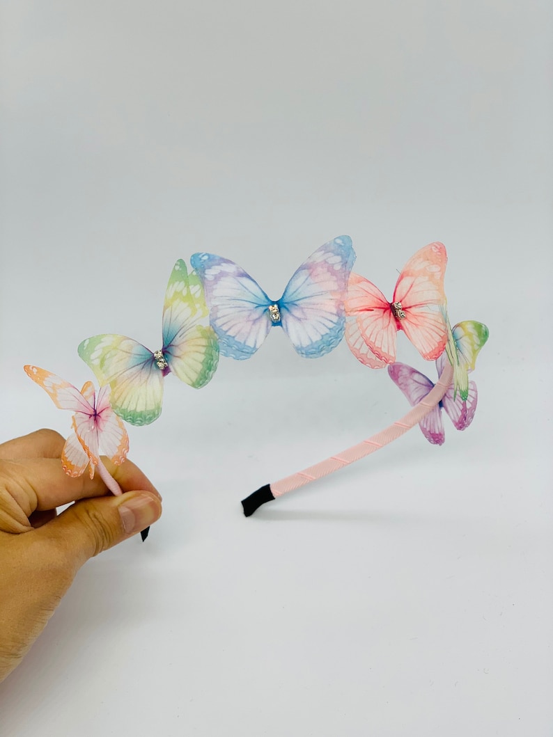 Pu&ograve; includere: Un cerchietto rosa con cinque fermagli per capelli a forma di farfalla iridescenti. Le farfalle sono in tonalit&agrave; di blu, rosa, verde e giallo.
