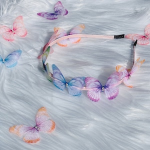 Pu&ograve; includere: Un cerchietto rosa con una fila di farfalle colorate. Le farfalle sono fatte di tessuto trasparente e hanno ali iridescenti.